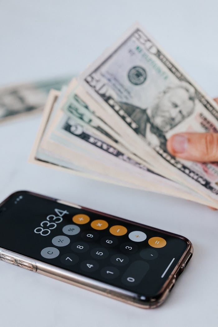 services-02 From above of crop anonymous person holding heap of American dollar near cellphone with calculator application representing numbers