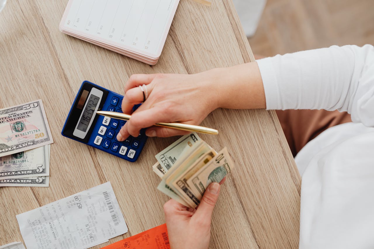 team-01 Person using a calculator and counting cash on a wooden table with receipts.