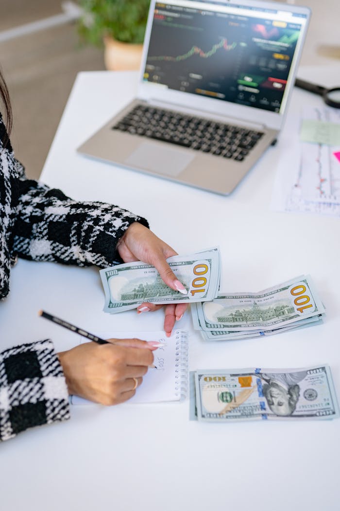 journey Woman counting American dollars with laptop and notes, focused on finance.