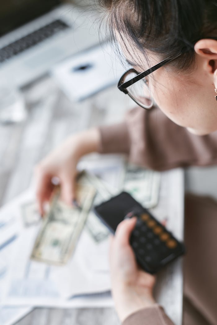 services-01 A woman calculates finances using a calculator with banknotes and documents on the table.